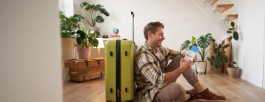 Yakışıklı genç bir adamın portresi, bavuluyla oturan bir turist, elinde pasaport ve uçak biletleri, tatile çıkıyor..