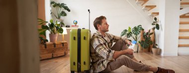 Gülümseyen yakışıklı turistin portresi, elinde pasaport ve uçak bileti olan bir adam, bavulla oturuyor. Turizm ve seyahat kavramı