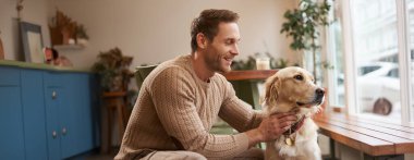 Genç yakışıklı köpek sahibi portresi, evcil hayvanıyla bir kafede vakit geçiriyor, içeride oturuyor, pencereden dışarı bakıyor..