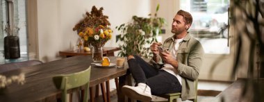 Gündelik giysiler içinde genç yakışıklı bir adamın portresi, kafede oturuyor ve en sevdiği şarkıyı seviyor, kablosuz kulaklıkla müzik dinliyor, kulaklıkla rahatlatıcı melodileri dinliyor, akıllı telefon tutuyor..