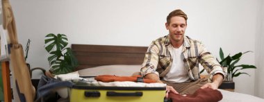 Genç bir adamın portresi, bavulları boşaltan gezgin, yatağa giysiler koyan, gülümseyen, tatilin tadını çıkaran, otelde kalan..