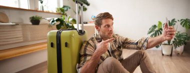 Yakışıklı mutlu adamın portresi, turistler bavulla selfie çeker, akıllı telefon kullanır. Turizm ve tatil konsepti