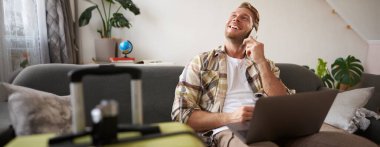 Bavul ve dizüstü bilgisayarlı gülümseyen genç adamın portresi, bir telefon görüşmesi yapmak, uçak bileti almak, otel odasını onaylamak için aramak. Boşluğu kopyala