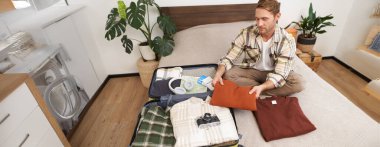 Genç bir turist resmi, yaz tatilinden sonra bavulunu boşaltan bir adam. Bagajlı bir adam, yatağa oturur, tatile gitmek için giysilerini toplar. Turizm, seyahat kavramı