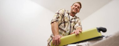 Kaslı, güçlü bir gencin alt açılı portresi. Elbiseleriyle dolu valizini kapatmaya çalışıyor. Çantasına gayretle bastırıyor. Turizm ve yaz tatili konsepti