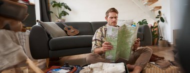 Genç bir adamın portresi, gezgin, bavulunu toplayan, seyahat haritasına bakan, tatil yerini seçen, tatilde güzergahı öğrenen. Turizm konsepti