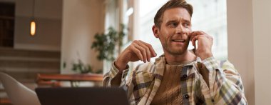 Genç işadamının portresi, şehirdeki kahve dükkanından uzaktan çalışan, dizüstü bilgisayarlı sandalyede oturan, bir telefona cevap veren, cep telefonuyla konuşan.