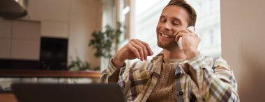 Genç profesyonel, kafeterya ziyaretçisi laptopla oturmuş müşteriyle cep telefonuyla konuşuyor. İnternetten bir şey alan, bir arkadaşını arayan bir adam..