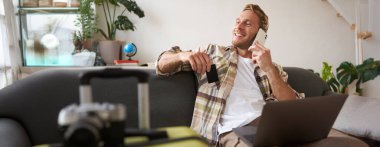 Cep telefonuyla konuşan gülümseyen adam, dizüstü bilgisayarla oturan, kredi kartı tutan, mutlu ve rahat bir yüz ifadesiyle pencereden dışarı bakan adam..