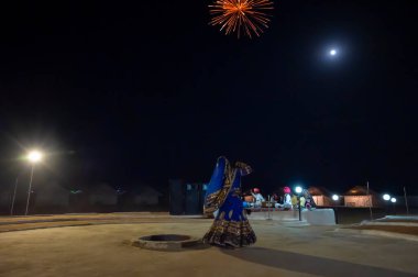 Thar desert, Rajasthan,India - October 15th 2019 : Rajasthani female, dancing in cultural dress of Rajasthan, at night. Musicians are playing in moonlit night with fire crackers bursting in night sky.