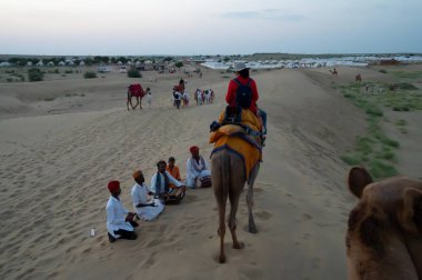 Thar Çölü, Rajassthan, Hindistan - 15 Ekim 2019: Thar Çölü 'nün kum tepelerinde deve sürüşü sırasında yerel halkla etkileşime geçen bir kadın turist. Deve binme turistler arasında favoridir..
