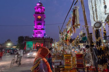 Jodhpur, Rajasthan, Hindistan - 19.10.2019: Altın ve gümüş kaplama süsler, bilezikler, mücevherler öğleden sonra ünlü Sardar Market ve Ghanta Ghar Saat Kulesinde satılıyor. Mavi saat.