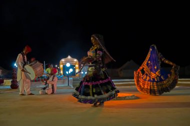 Thar desert, Rajasthan, India - October 15th 2019 : Rajasthani female dancer dancing, dressed with cultural dress of Rajasthan, at night. Male Musicians are playing music instruments in background.