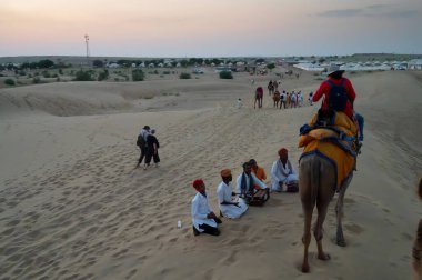 Thar Çölü, Rajassthan, Hindistan - 15 Ekim 2019: Thar Çölü 'nün kum tepelerinde deve sürüşü sırasında yerel halkla etkileşime geçen bir kadın turist. Deve binme turistler arasında favoridir..