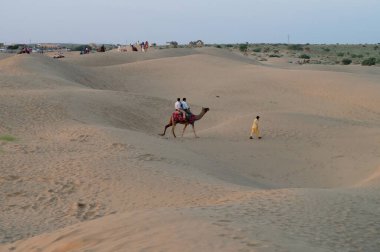 Tourists riding camels, Camelus dromedarius, at sand dunes of Thar desert, Rajasthan, India. Camel riding is a favourite activity amongst all tourists visiting here.