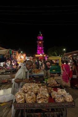 Jodhpur, Rajasthan, Hindistan - 20.10.2019: Rajasthani sokak yemekleri geceleyin ünlü Sardar Market ve Hindistan 'ın Jodhpur kentindeki Ghanta ghar saat kulesinde yol kenarı gıda tezgahlarında satılıyor.