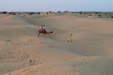 Tourists riding camels, Camelus dromedarius, at sand dunes of Thar desert, Rajasthan, India. Camel riding is a favourite activity amongst all tourists visiting here.