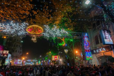 Kolkata, Batı Bengal, Hindistan - 25.12.2018: Aydınlanmış ve dekore edilmiş park caddesinde yıl sonu şenlik havasında eğlenen gençler. Gece gökyüzü arkaplanı.