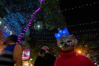 Kolkata, Batı Bengal, Hindistan - 25.12.2018: Aydınlanmış ve dekore edilmiş park caddesinde yıl sonu şenlik havasında eğlenen gençler. Renkli güzel maskeli kadın.