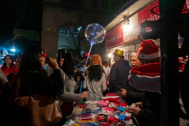 Kolkata, Batı Bengal, Hindistan - 25.12.2018: Gençler yol kenarındaki tezgahtan kırmızı şapkalar ve diğer festival hediyeleri alıyor ve aydınlık ve dekore edilmiş park caddesinde neşeli bir şekilde eğleniyorlar.