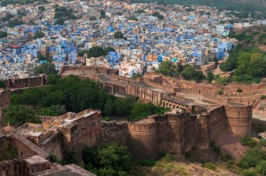 Top view of Mehrangarh fort with distant view of blue city Jodhpur, Rajasthan, India. Blue sky with white clouds in the background. One of the seven gates to enter the huge fort is seen below,