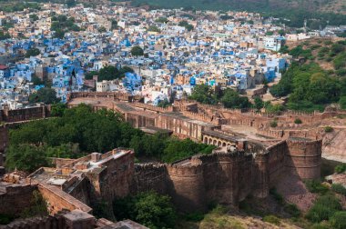 Top view of Mehrangarh fort with distant view of blue city Jodhpur, Rajasthan, India. Blue sky with white clouds in the background. One of the seven gates to enter the huge fort is seen below,