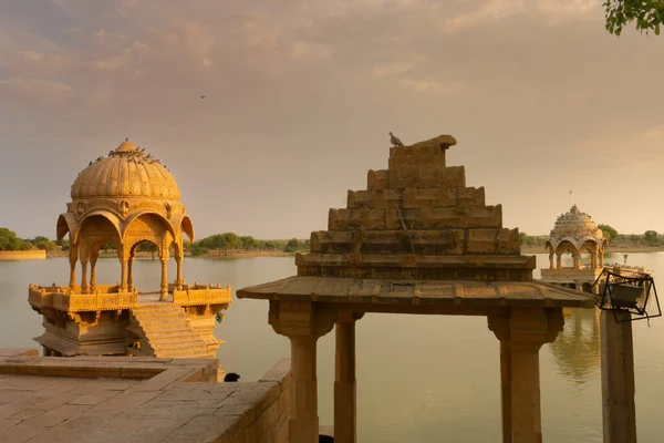 Chhatris and shrines of hindu Gods and goddesses at Gadisar lake, Jaisalmer, Rajasthan, India. Indo-Islamic architecture , sun set and colorful clouds in the sky with view of the Gadisar lake.