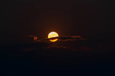 The orange moon, also known as the harvest moon or the hunter's moon, over the night sky at Sikkim, India. Moon is partly covered by clouds.