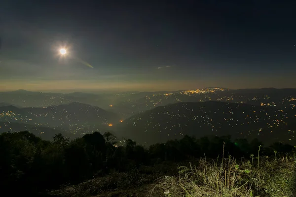 Pearls of light of Queen of Hills, Darjeeling town, at night at far right. Full moon on the night sky shows of mountains of Eastern Himalays with ridges and localities of Sikkim, West Bengal, India.