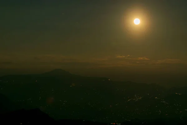 Rise of the orange moon, also known as the harvest moon or the hunter\'s moon, over the night sky at Sikkim, India. Moon orange due to atmosphere.Sikkim at night is seen below with Himalayan mountains.