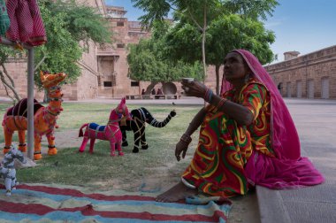 Jodhpur, Rajasthan, India - 19th October 2019 : Old aged Rajasthani woman selling hand made Rajaasthani colourful dolls of horse and elephant. Rajasthan is famous for its vibrant colors all across.