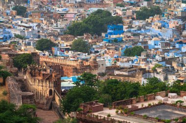 Top view of Mehrangarh fort with distant view of blue city Jodhpur, Rajasthan, India. Blue sky with white clouds in the background. One of the seven gates to enter the huge fort is seen below,