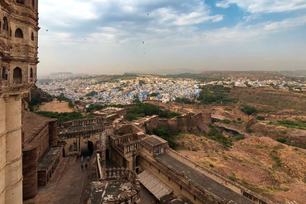 View of Mehrangarh fort with distant view of blue city Jodhpur, Rajasthan, India. Historical Fort is UNESCO world heritage site. Blue sky with white clouds in the background.