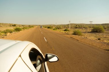 Thar Çölü, Rajasthan, Hindistan - 15.10.2019: Beyaz araba boş anayolda ya da çölden geçen ulusal otoyolda ilerliyor. Uzak ufuk, Sıcak yaz.