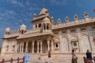 Jodhpur, Rajasthan, Hindistan - 20.10.2019: Jaswant Thada Cenotaph 'ın güzel mimarisinin fotoğrafını çeken gezginler. Makrana mermeri güneş tarafından aydınlatıldığında sıcak parıltı yayar. Mavi gökyüzü arkaplanı.