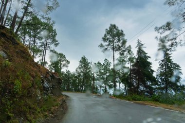 Bulutlu gökyüzü ve Himalaya yolunun kıvrımları, Garhwal muson manzarası, Uttarakhand, Hindistan. Himalayalar üzerindeki iklim değişikliği etkisi toprak kayması, zamansız yağmur ve dağ çevresinin tahrip edilmesine yol açıyor.