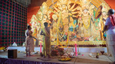 Howrah, Batı Bengal, Hindistan - 5 Ekim 2022: Hindu Purohit 'ler Durga' ya tapıyor, büyük bir yelpazeyle onu Durga Puja pandalının içinde havalandırıyor. Durga Puja ayini. Hinduizm Festivali.