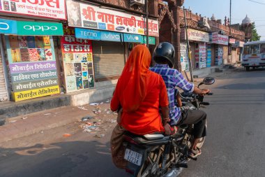 Jodhpur, Rajasthan, Hindistan - 15.10.2019: Şehir yolunda bisiklet süren kırmızı elbiseli kadın. Rajasthan renkleriyle ünlüdür..