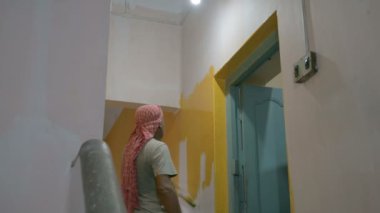 Howrah, Batı Bengal, Hindistan - 06.08.2023: Eski evin soluk duvarına sarı renk boyamak için fırça kullanan Hintli ressam. Renkli ev duvarları için iç mekan boyama.