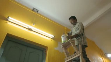 Howrah, Batı Bengal, Hindistan - 06.08.2023: Eski evin soluk duvarına sarı renk boyamak için fırça kullanan Hintli ressam. Renkli ev duvarları için iç mekan boyama.