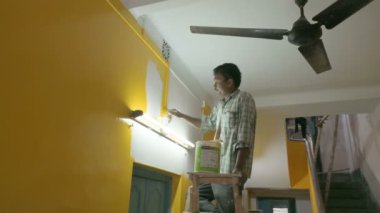 Howrah, Batı Bengal, Hindistan - 06.08.2023: Eski evin soluk duvarına sarı renk boyamak için fırça kullanan Hintli ressam. Renkli ev duvarları için iç mekan boyama.