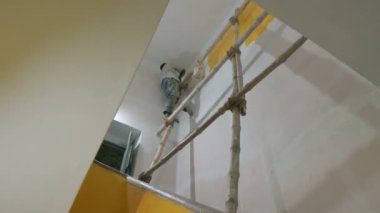 Howrah, Batı Bengal, Hindistan - 06.08.2023: Eski evin soluk duvarına sarı renk boyamak için fırça kullanan Hintli ressam. Renkli ev duvarları için iç mekan boyama.