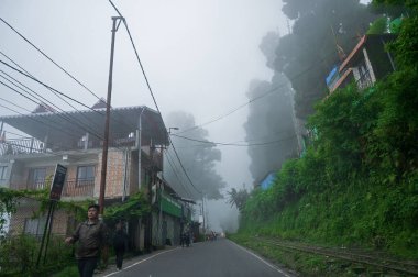 Kurseong, Batı Bengal, Hindistan - 10 Ağustos 2023: Evler ve Himalaya dağları ve yemyeşil ormanlarından geçen beton bir yol. Kurseong, Darjeeling bölgesinde muson yağmurlarının doğal güzelliği.
