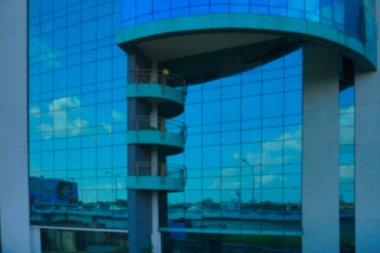 Binaların modern mimarisinin bulanık görüntüsü, mavi gökyüzünü yansıtan cam dış görünüş, beyaz bulutlar ve binalar..