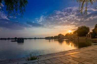 Beautiful sunset at Gadisar lake, Jaisalmer, Rajasthan, India. Setting sun and colorful clouds in the sky with view of the Gadisar lake. Connected with Indira Gandhi Canal for continuous water supply.