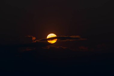 The orange moon, also known as the harvest moon or the hunter's moon, over the night sky at Sikkim, India. Moon is partly covered by clouds.