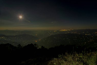 Pearls of light of Queen of Hills, Darjeeling town, at night at far right. Full moon on the night sky shows of mountains of Eastern Himalays with ridges and localities of Sikkim, West Bengal, India. clipart