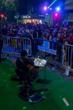 Kolkata, West Bengal, India - 25.12.2018 : Street singer singing festive mood songs while young people enjoying themselves at illuminated and decorated park street with year end joy and festive mood. clipart