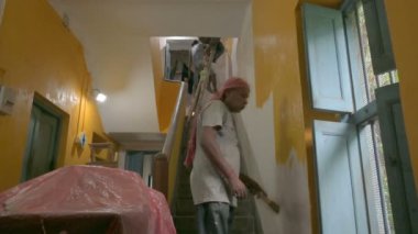 Howrah, Batı Bengal, Hindistan - 06.08.2023: Hintli ressamlar eski evlerinin solmuş duvarlarına sarı renk boyamak için fırça kullandılar. Renkli ev duvarları için içeriyi boyamak için el işçiliği.