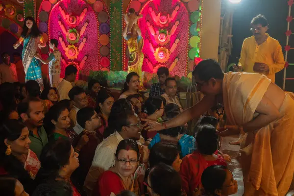 stock image Howrah,West Bengal,India- 3rd October, 2022 : Hindu purohit drawing tilak, holy sign on forehead of Hindu devotees worshipping Goddess Durga, inside decorated Durga Puja Pandal at night. Durga puja.